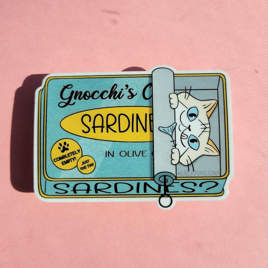 Sticker of a cat peeking out from a sardine can labeled 'Gnocchi's' on a pink background