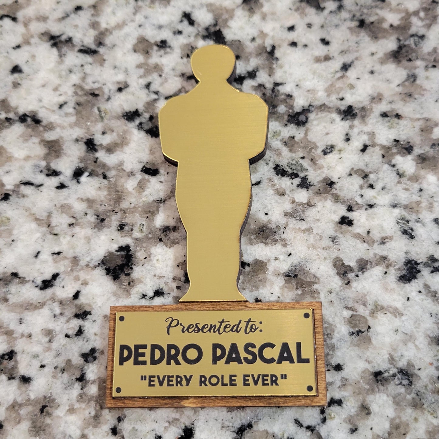 gold and dark stained wood in the shape of an oscar award on a granite surface