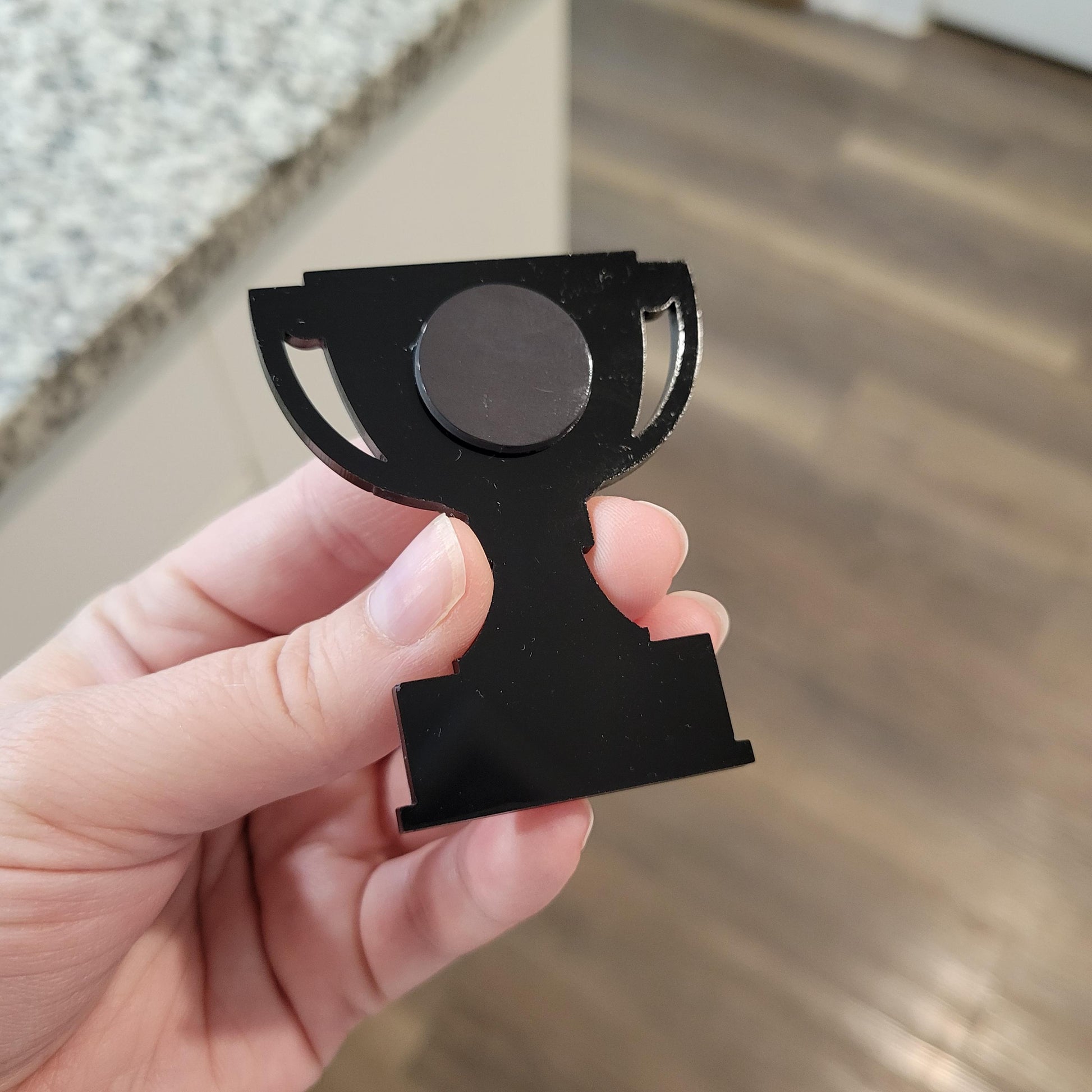 Black trophy-shaped magnet held in a hand with a blurred background