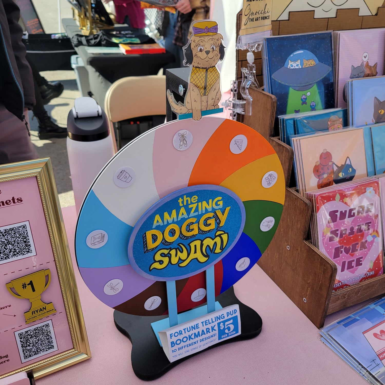 Colorful wheel with 'The Amazing Doggy Swim' logo on a pink surface with books and toys.