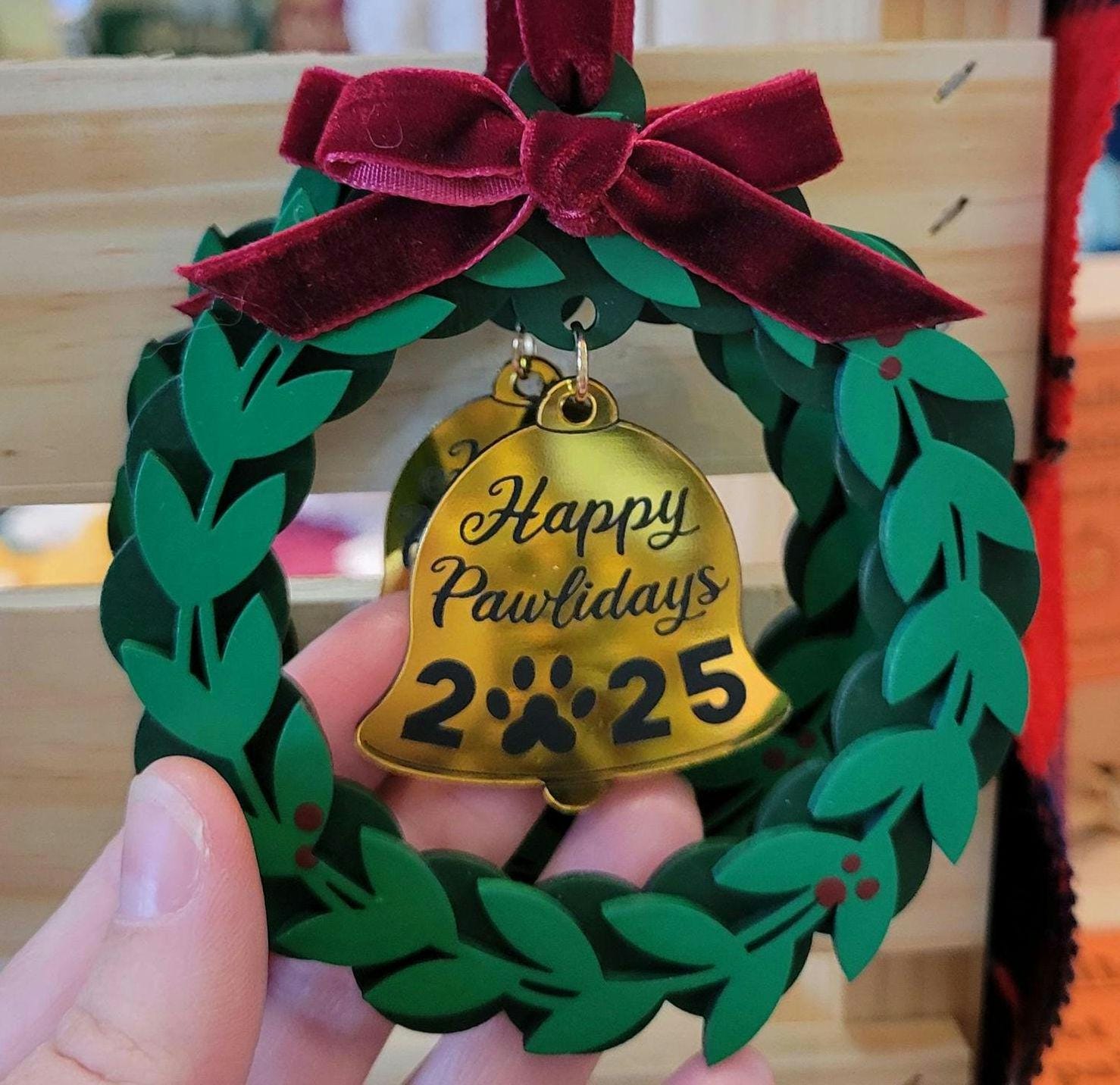 Decorative ornament with a gold bell and green wreath, featuring 'Happy Pawlidays 2025'.