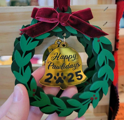Decorative ornament with a gold bell and green wreath, featuring 'Happy Pawlidays 2025'.