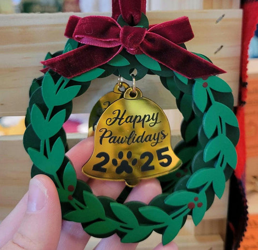 Decorative ornament with a gold bell and green wreath, featuring 'Happy Pawlidays 2025'.