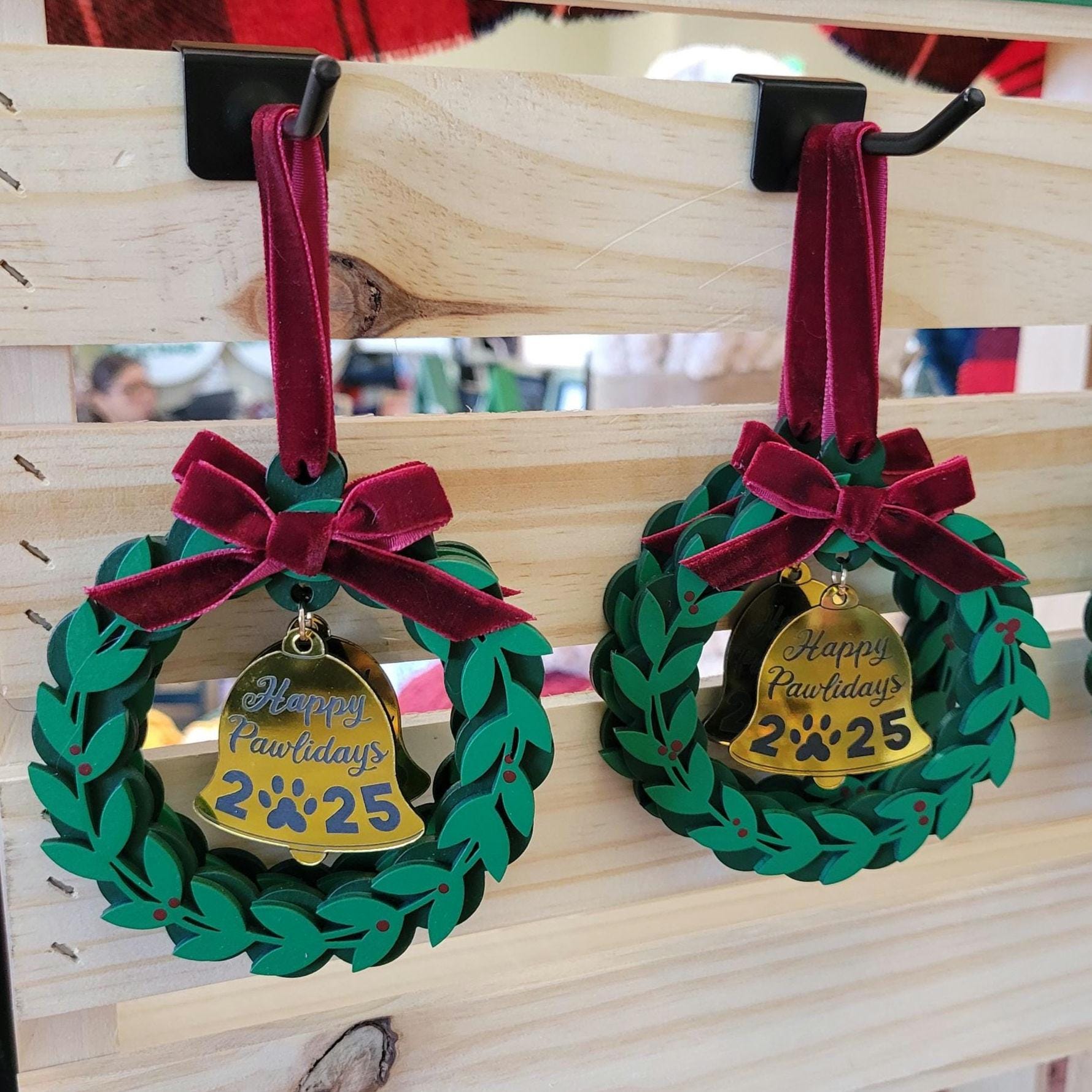 Two green wreath ornaments with red bows and gold tags on a wooden surface.