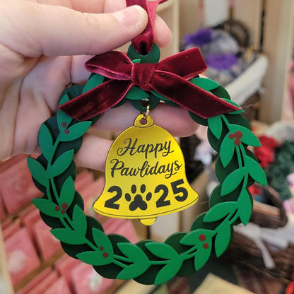 Christmas ornament with green wreath, red bow, and yellow bell reading 'Happy Pawlidays 2025'
