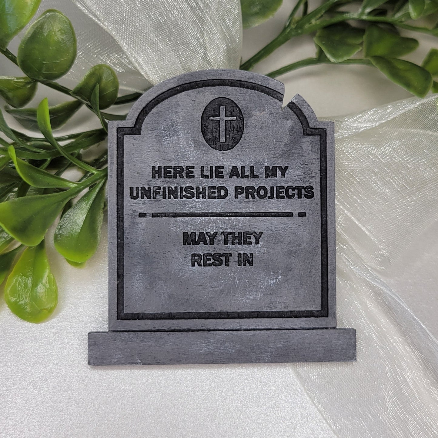 Wooden painted tombstone with words 'here lie all my unfinished projects may they rest in'