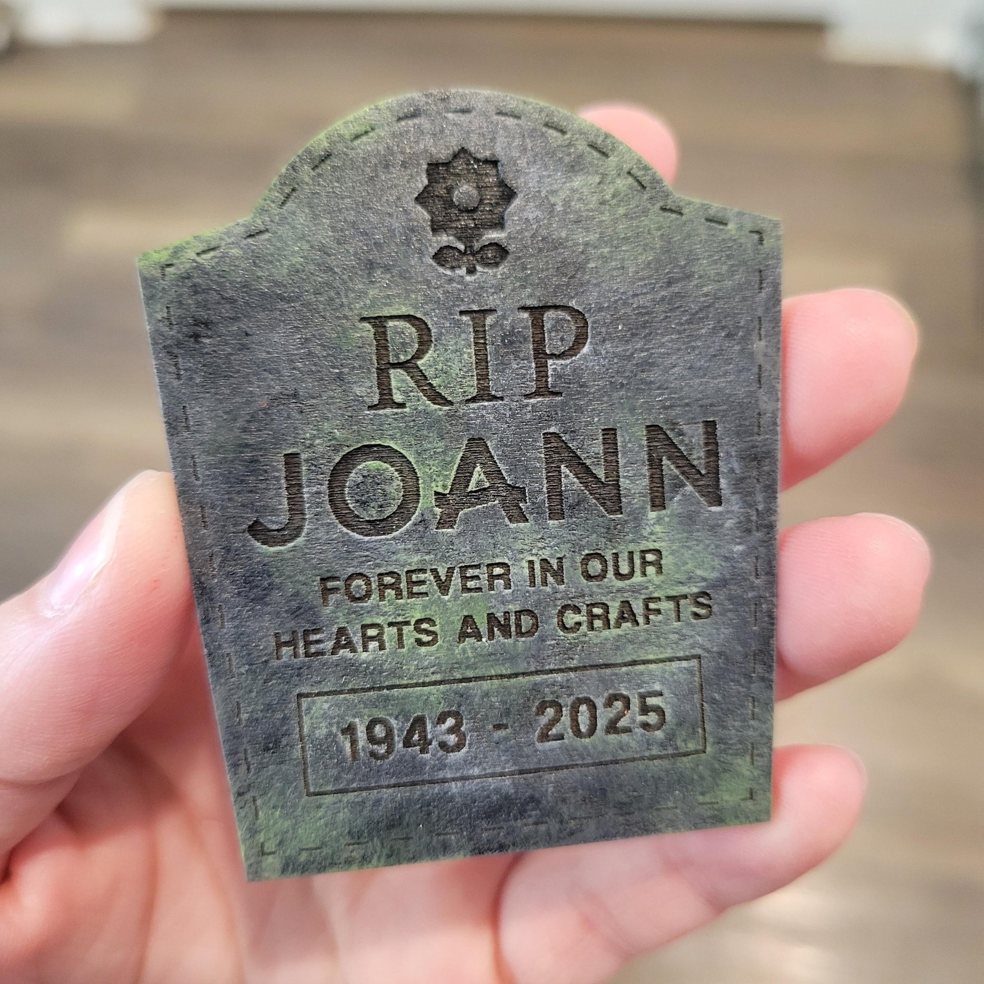 Memorial tombstone with 'RIP JOANN' held in a hand.