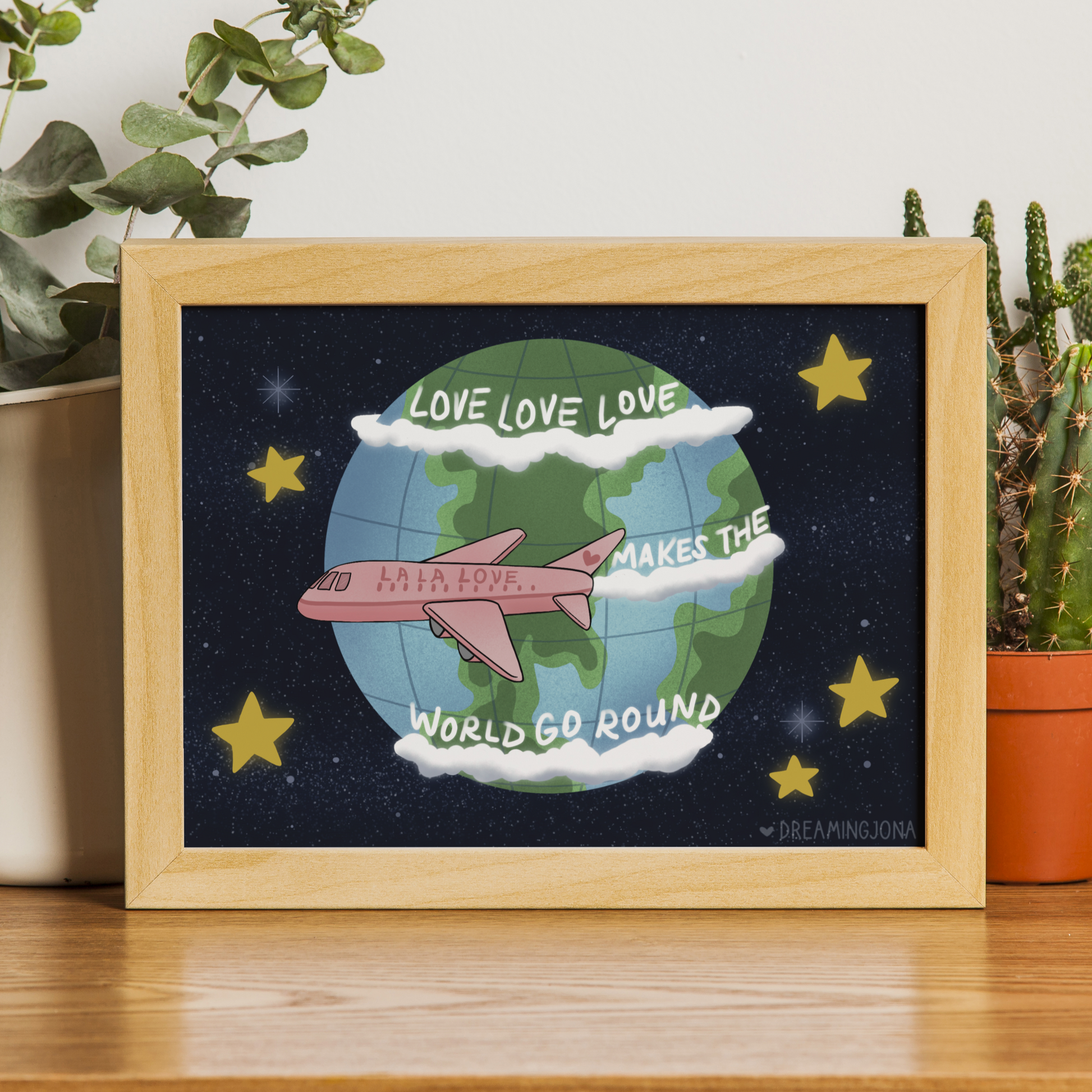 Framed artwork with airplane and globe design on a wooden surface with plants in the background