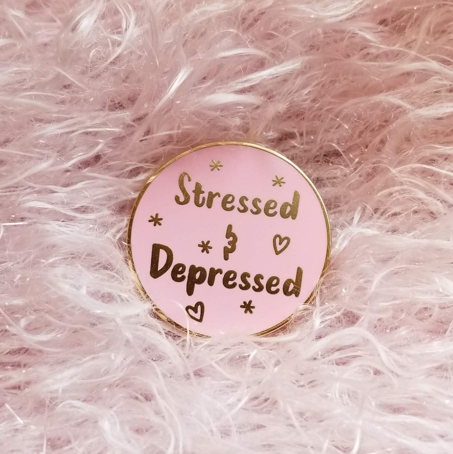 Pink enamel pin with 'Stressed & Depressed' text on a pink fluffy background