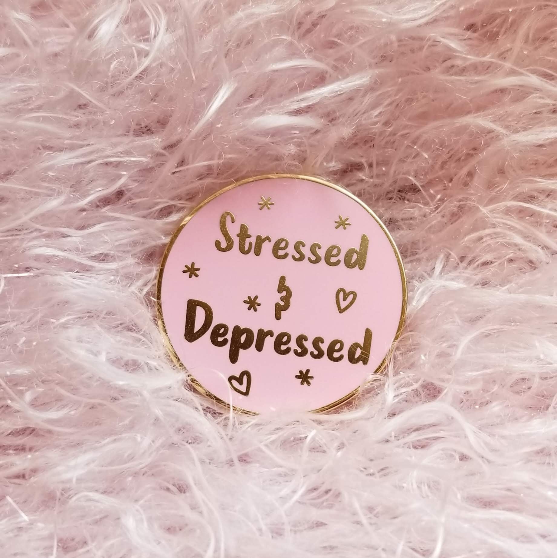 Pink enamel pin with 'Stressed & Depressed' text on a pink fluffy background
