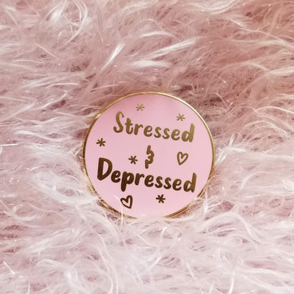 Pink enamel pin with 'Stressed & Depressed' text on a pink fluffy background