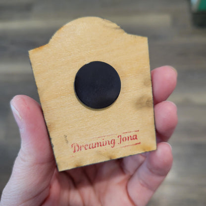 Hand holding a wooden tombstone with a magnet on the back