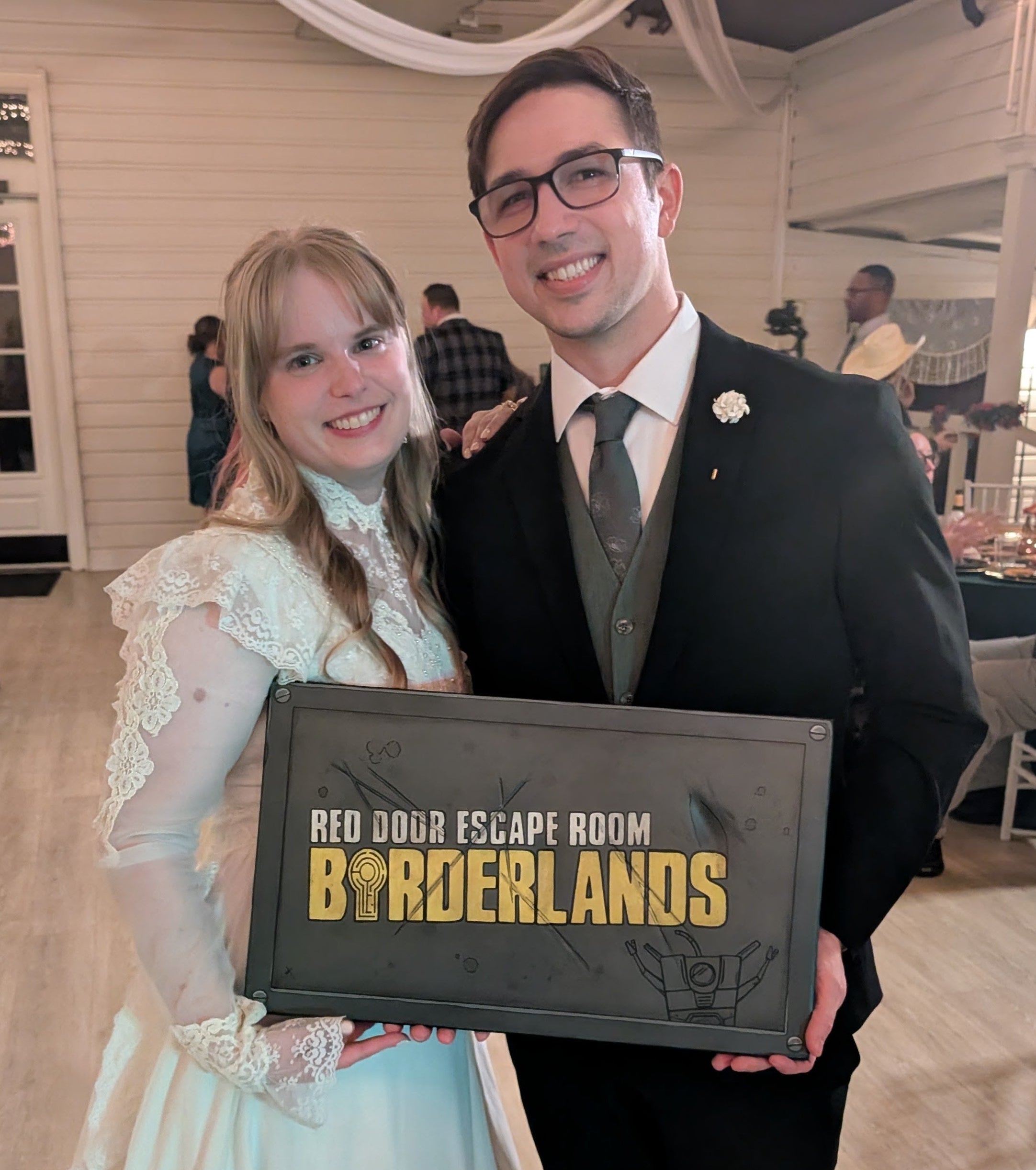 Man and woman holding a 'Red Door Escape Room Borderlands' sign in an indoor setting.