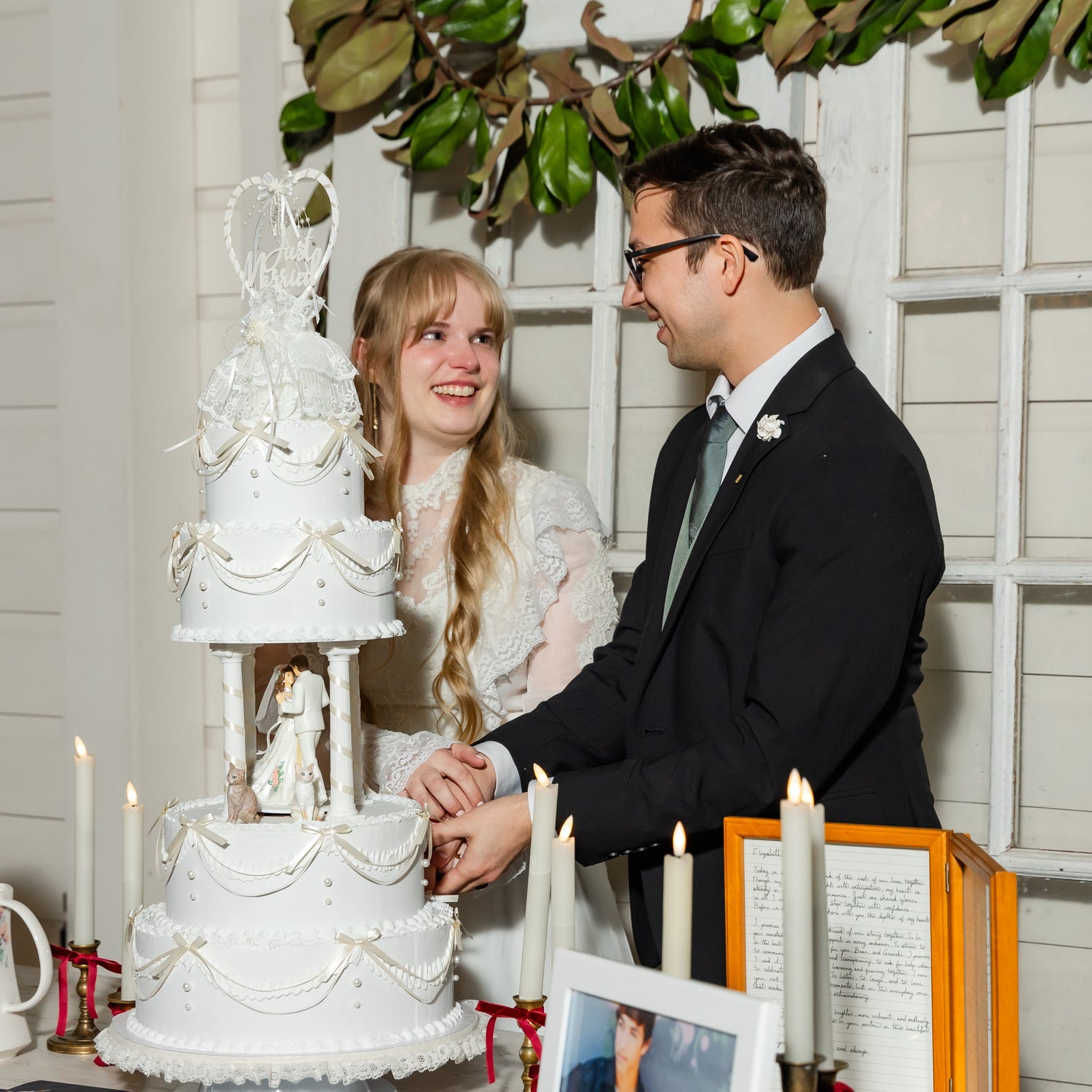Couple cutting a wedding cake with decorative elements and candles in the background.