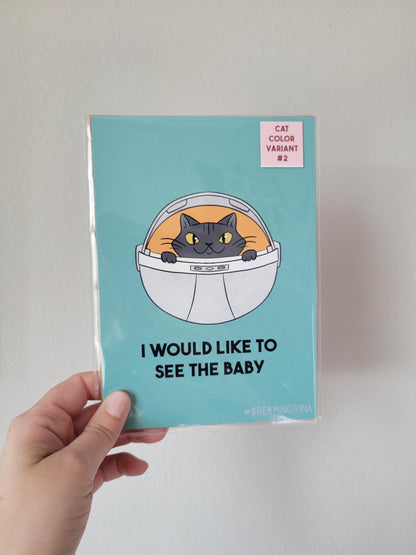 Card with a cat in an astronaut helmet illustration and text held by a hand against a light gray background