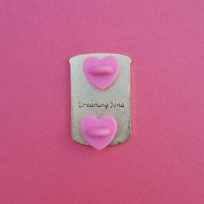 Decorative pin with pink backing posts and 'Dreaming Jona' text on a pink background