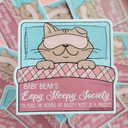 Sticker of a bear in bed with a sleep mask, surrounded by more stickers with similar designs.