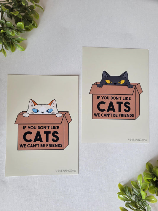 Two posters with cat illustrations and text on a white surface with green plants.