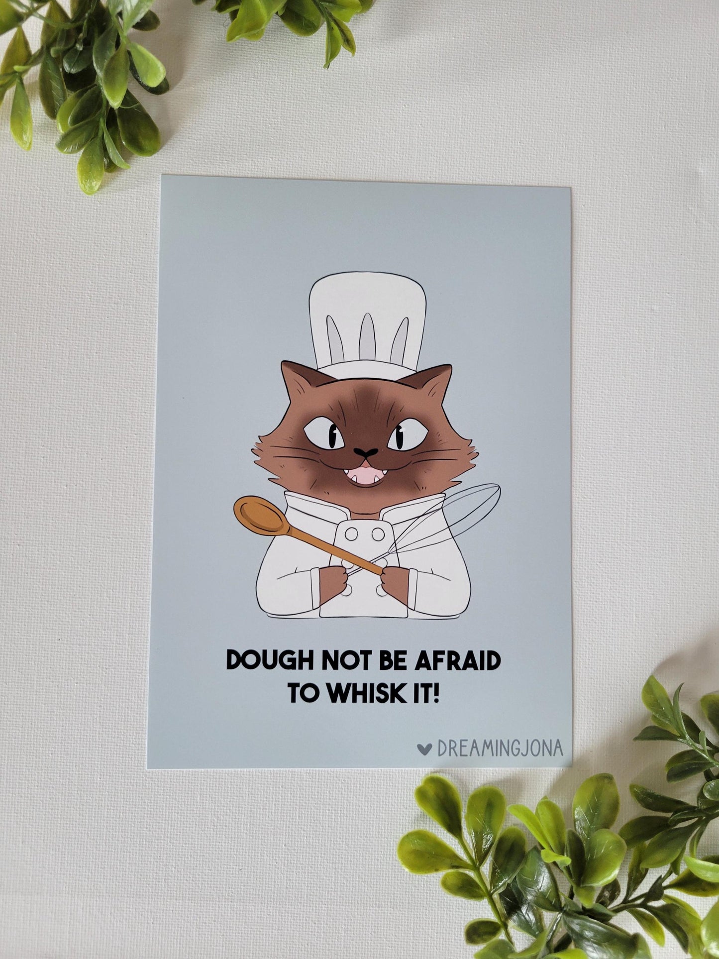 Siamese cartoon cat chef holding a wooden spoon with text on a light blue background, surrounded by green plants.