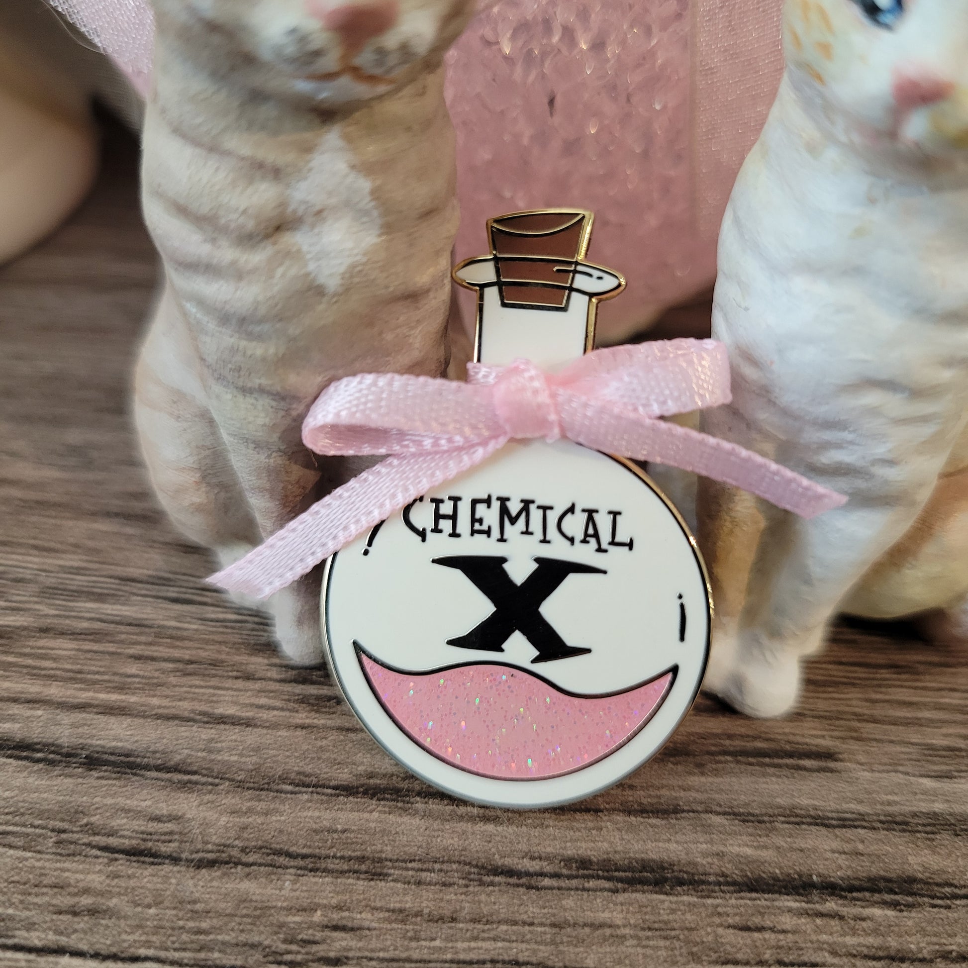 Small round object with a pink ribbon and 'Chemical X' text on a wooden surface