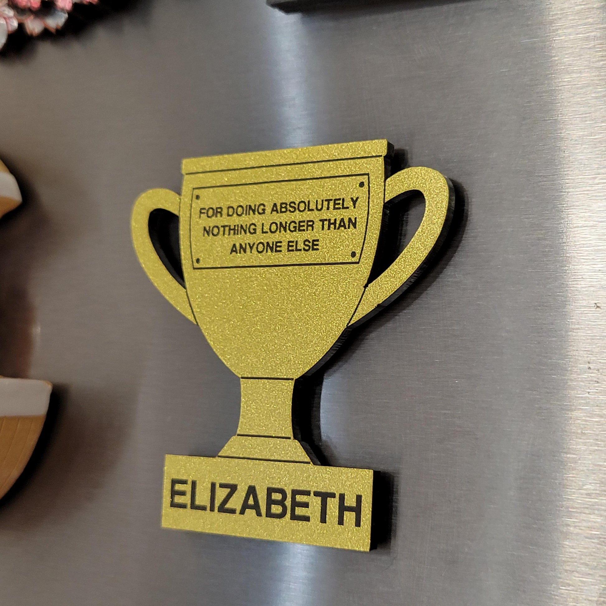 Gold trophy-shaped magnet with humorous text on a fridge