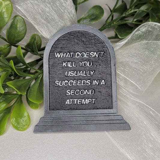 Decorative tombstone plaque with text on a white ribbon and green leaves