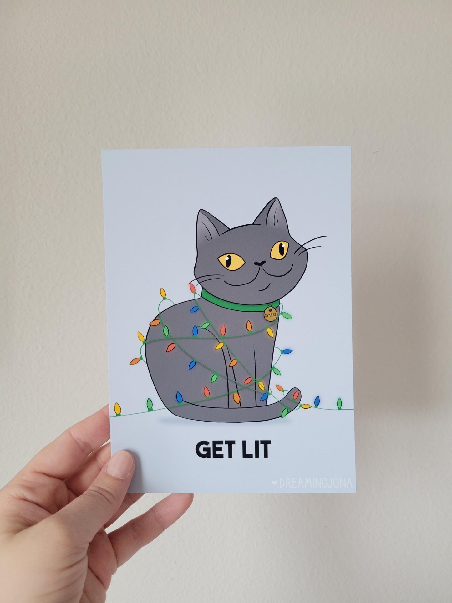 Card with a cat illustration and 'GET LIT' text held by a hand against a plain background