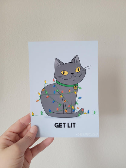 Card with a cat illustration and 'GET LIT' text held by a hand against a plain background