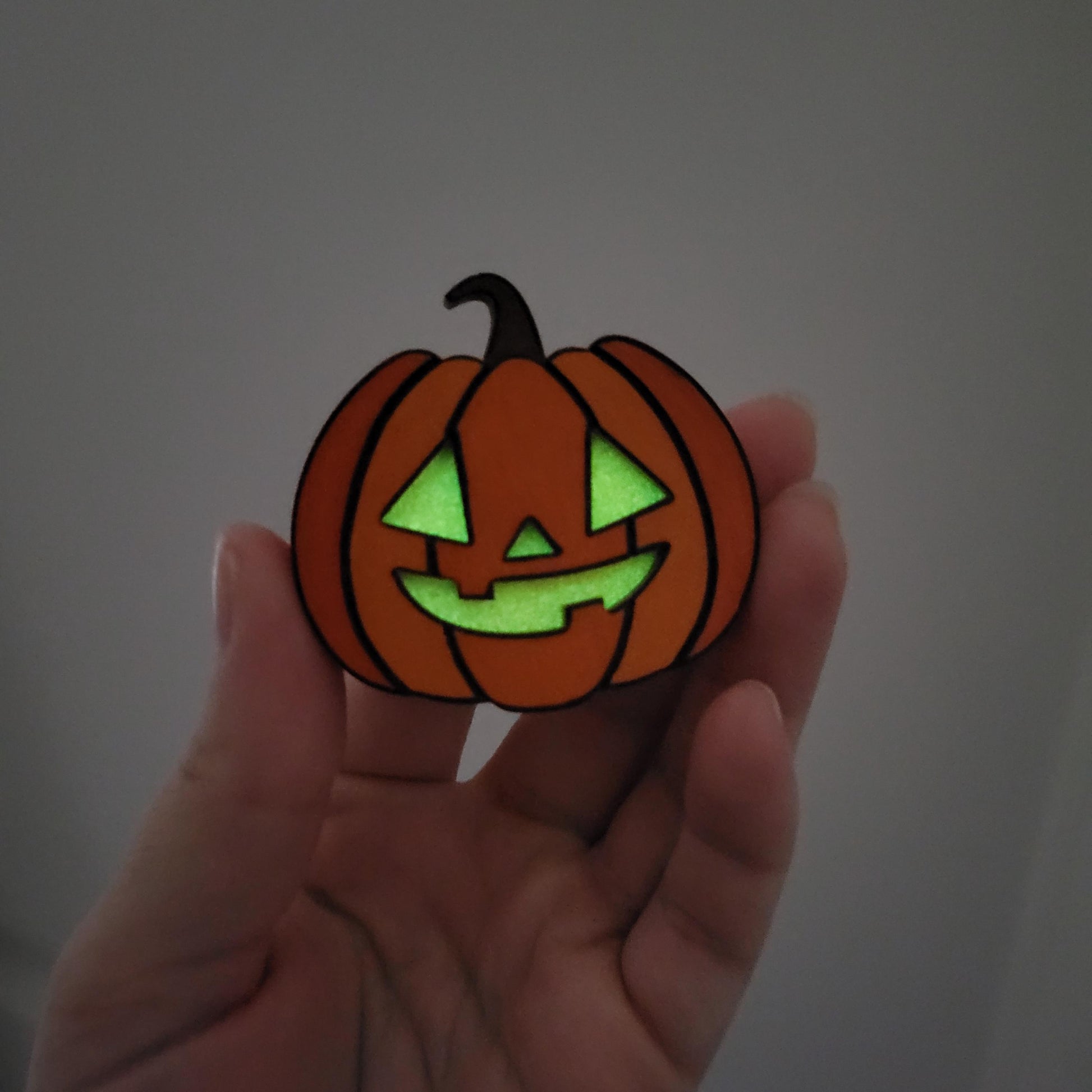 Hand holding a small pumpkin-shaped object with glowing green face on a plain background
