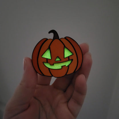 Hand holding a small pumpkin-shaped object with glowing green face on a plain background