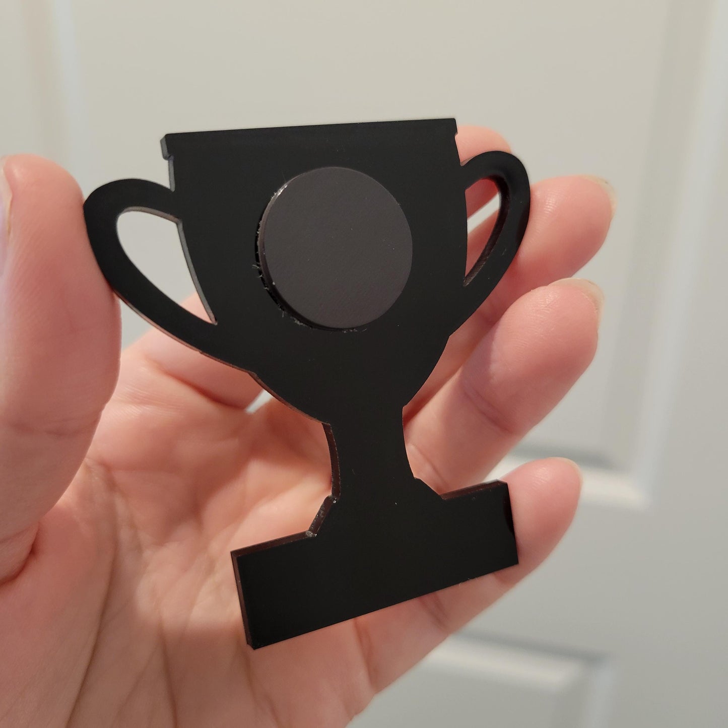 Black trophy-shaped magnet held in a hand against a neutral background