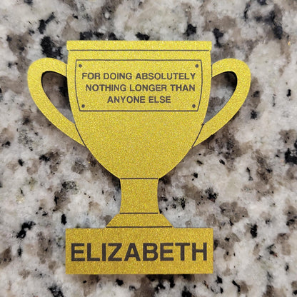 Gold trophy-shaped sign with humorous text on a granite surface