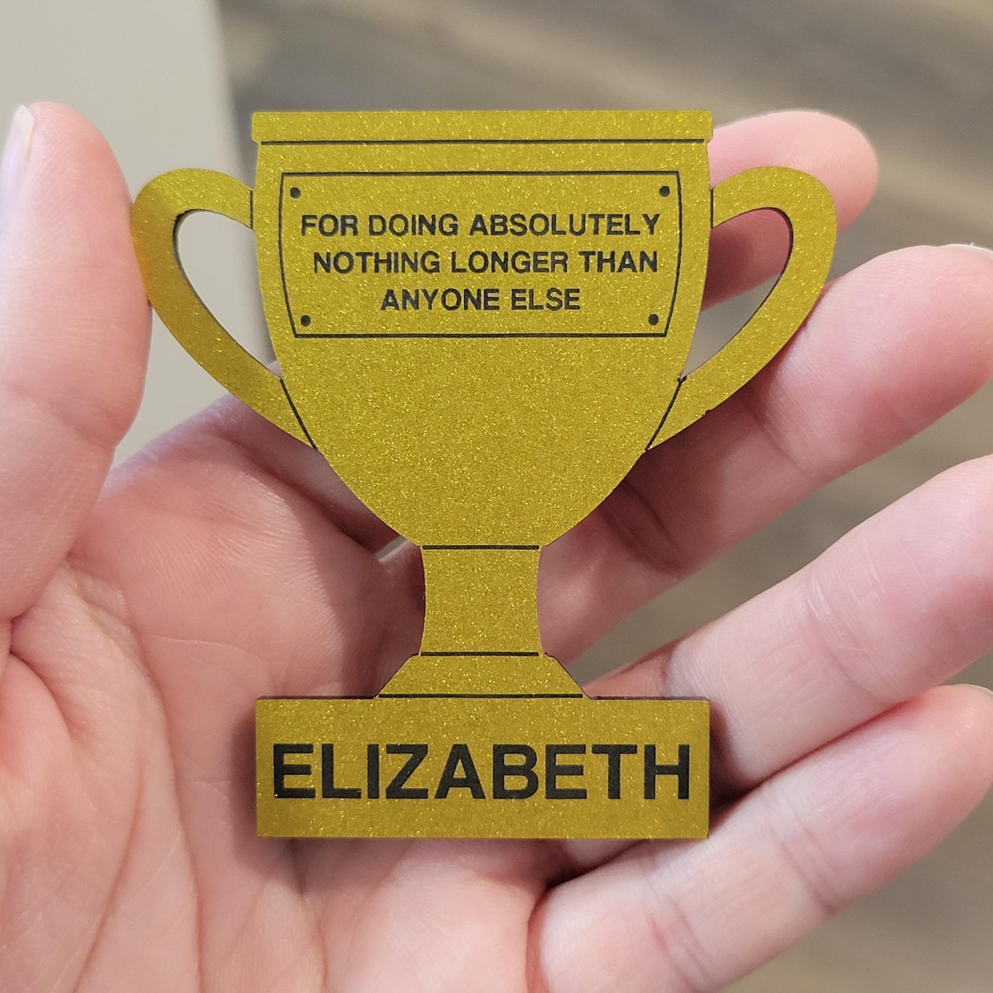 Gold trophy-shaped award with humorous text held in a hand
