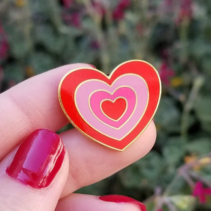 Heart-shaped pin with red and pink hearts held between fingers against a blurred natural background
