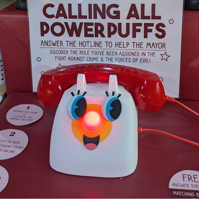 Display with a Powerpuff Girls-themed phone, candelabras, and a sign in an outdoor setting.