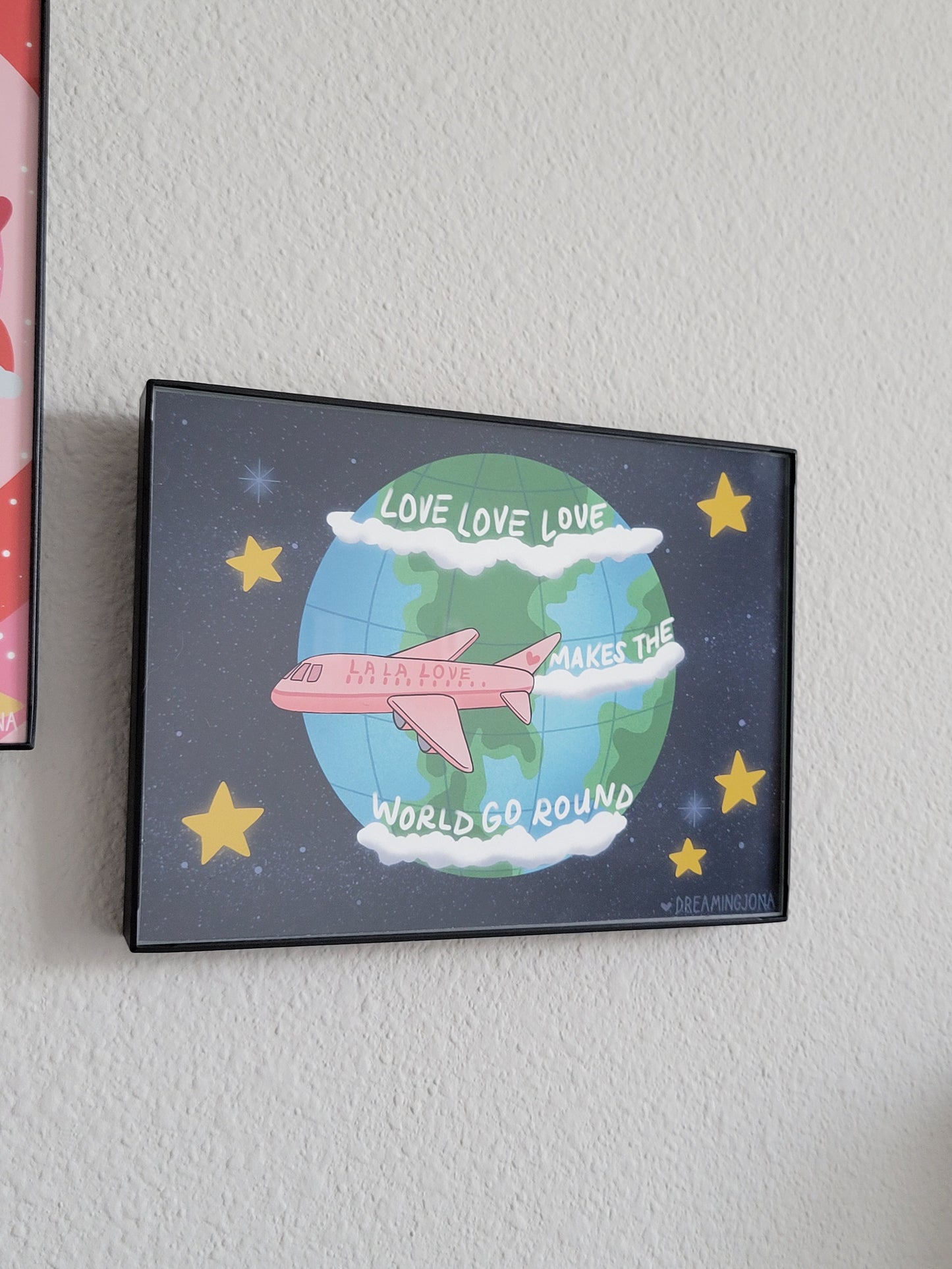 Framed artwork with a pink airplane on a globe against a starry background.