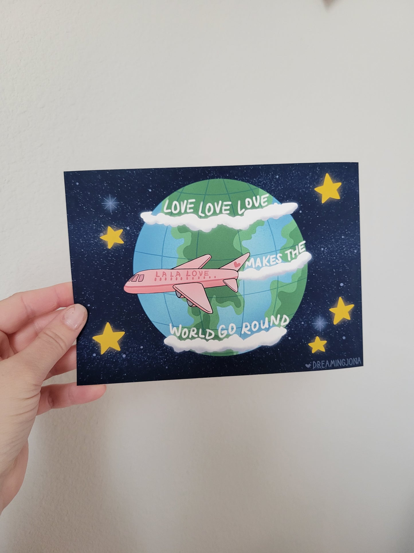 Hand holding a postcard with a world map and airplane design against a starry night sky.