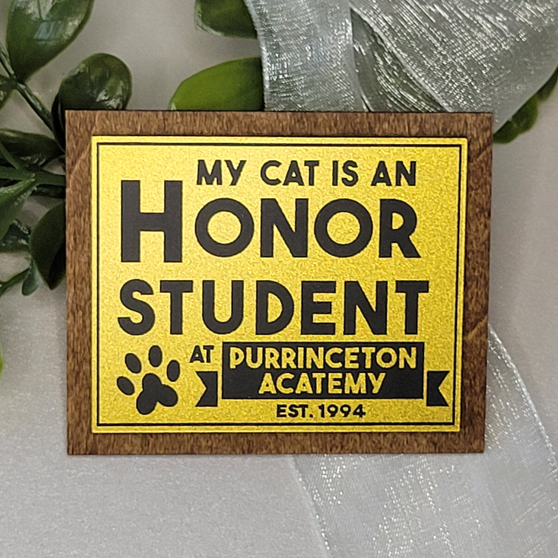 Wooden sign with gold and black text about a cat being an honor student at Purrinceton Academy.