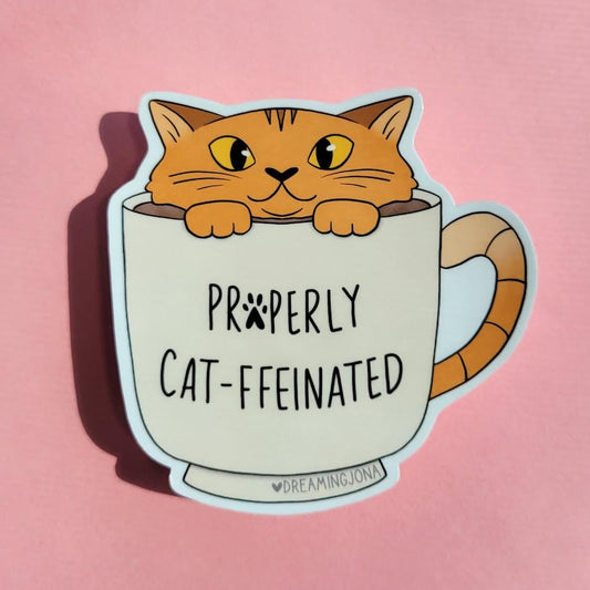 Sticker of a cat in a mug with 'Properly Cat-ffeinated' text on a pink background