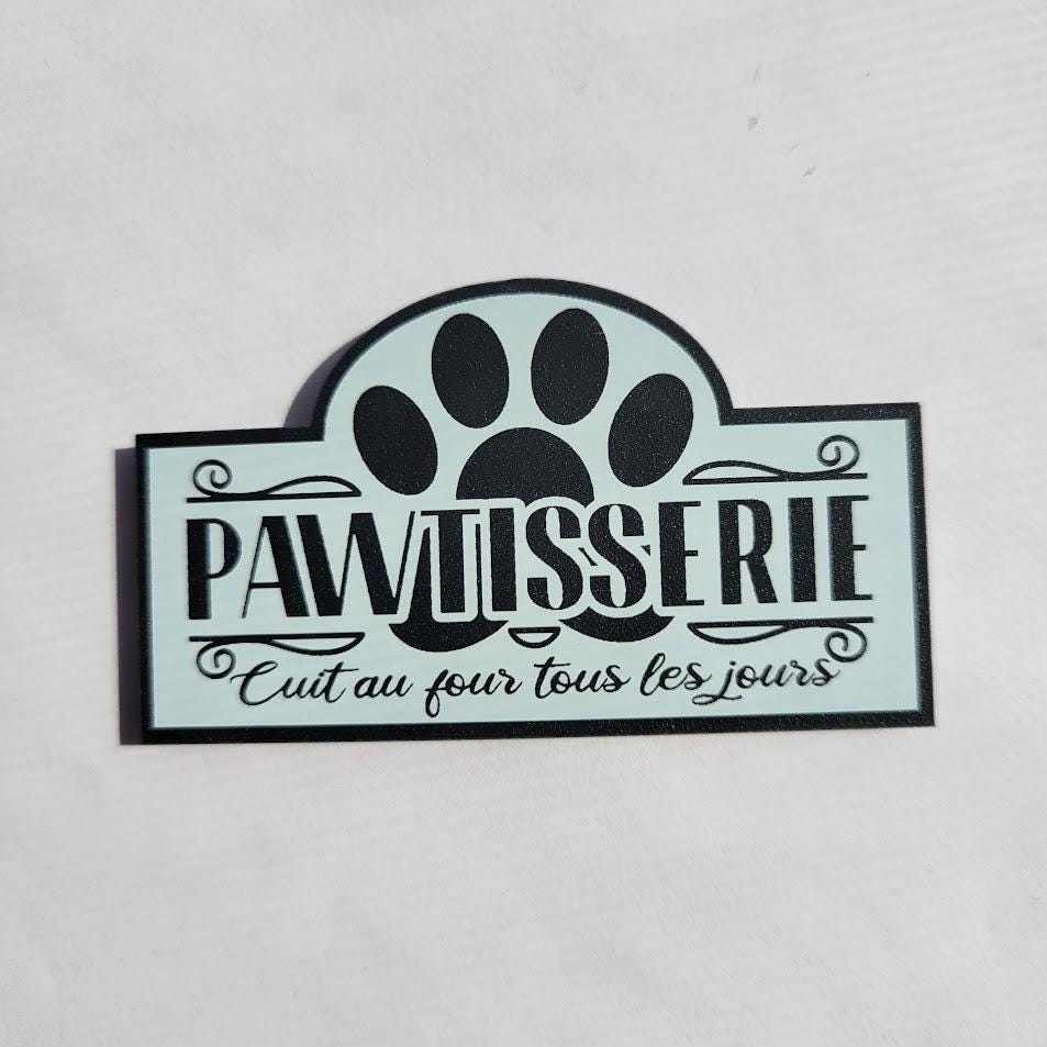 Decorative sign with paw print and text 'pawtisserie' on a light gray background