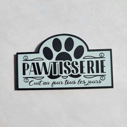 Decorative sign with paw print and text 'pawtisserie' on a light gray background