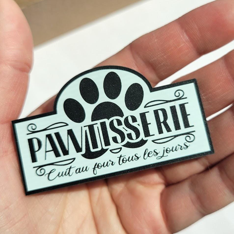 Paw-shaped sign with 'pawtisserie' text held in a hand