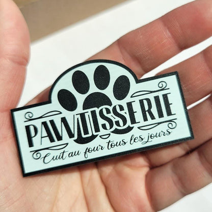Paw-shaped sign with 'pawtisserie' text held in a hand