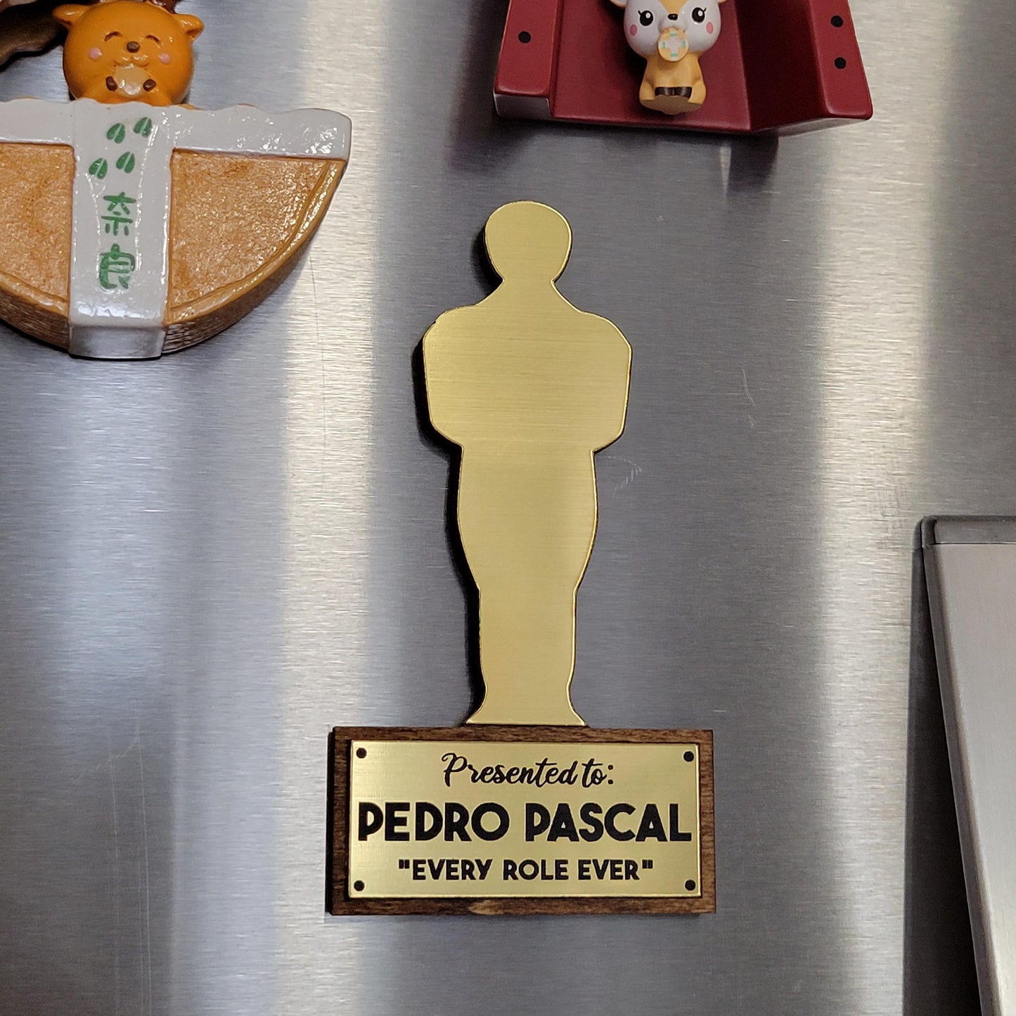 Gold Oscar statue-shaped magnet on a refrigerator with text 'Presented to: Pedro Pascal 'Every Role Ever'.'