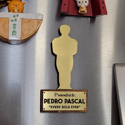 Gold Oscar statue-shaped magnet on a refrigerator with text 'Presented to: Pedro Pascal 'Every Role Ever'.'
