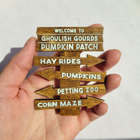 Hand holding a wooden sign with text about a pumpkin patch and related activities.