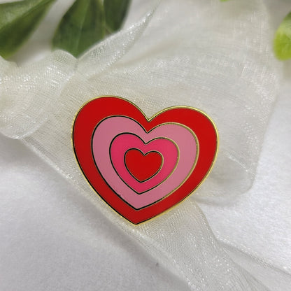 Heart-shaped pink and red object on a white fabric background with green leaves.