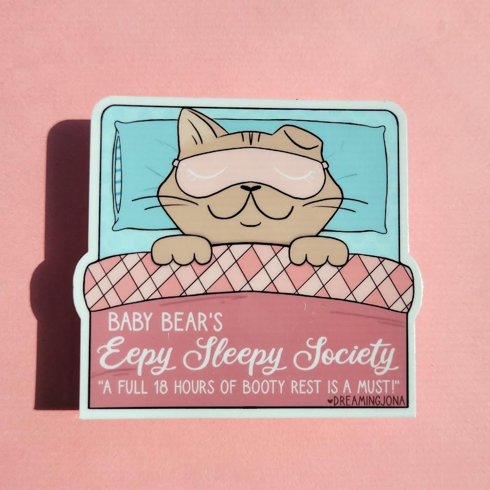 Sticker of a bear in bed with a sleep mask on a pink background, featuring text about sleep.