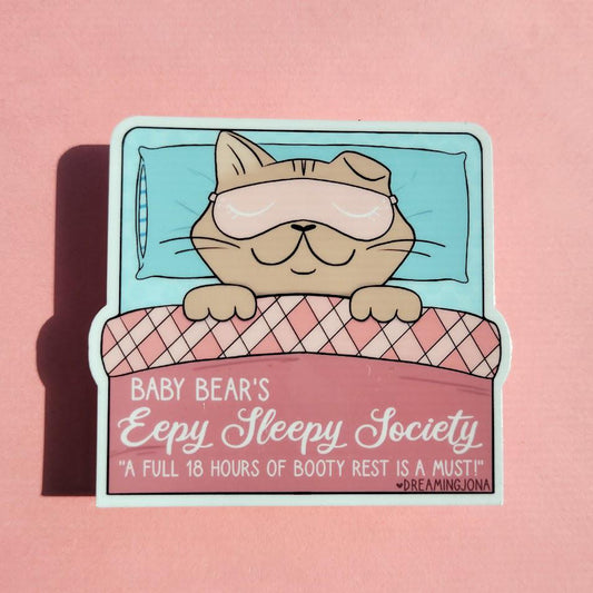 Sticker of a bear in bed with a sleep mask on a pink background, featuring text about sleep.