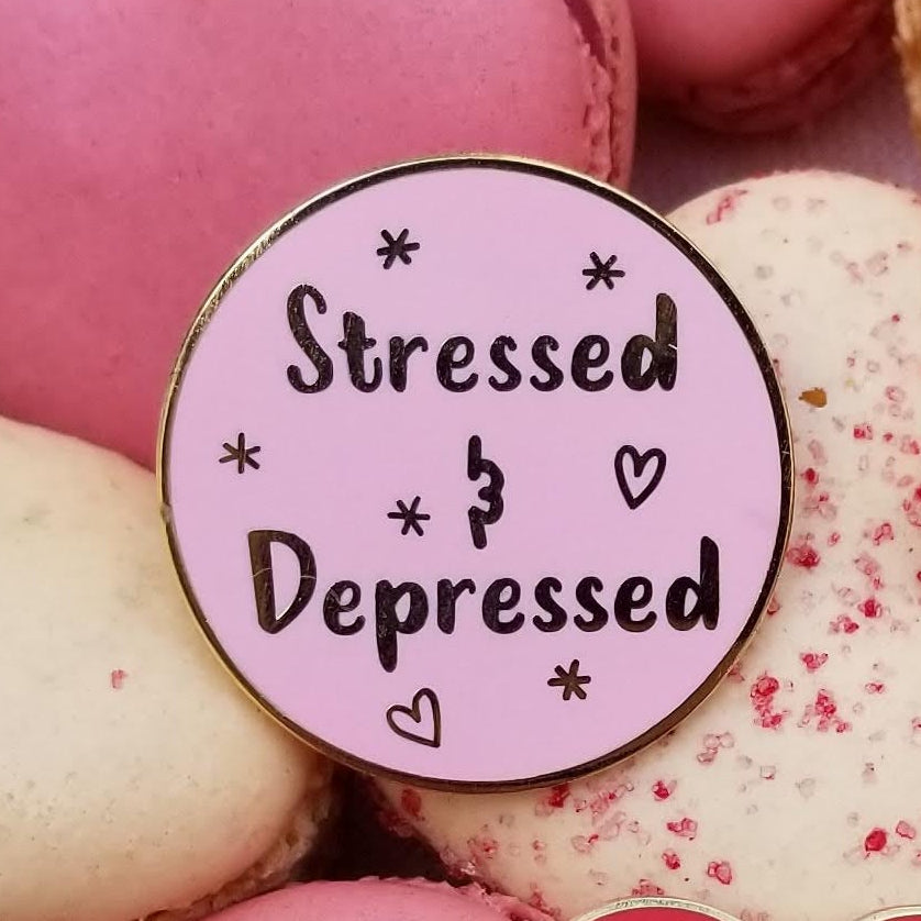 Heart-shaped macarons on a pink checkered towel with a pink enamel pin that reads 'stressed and depressed'